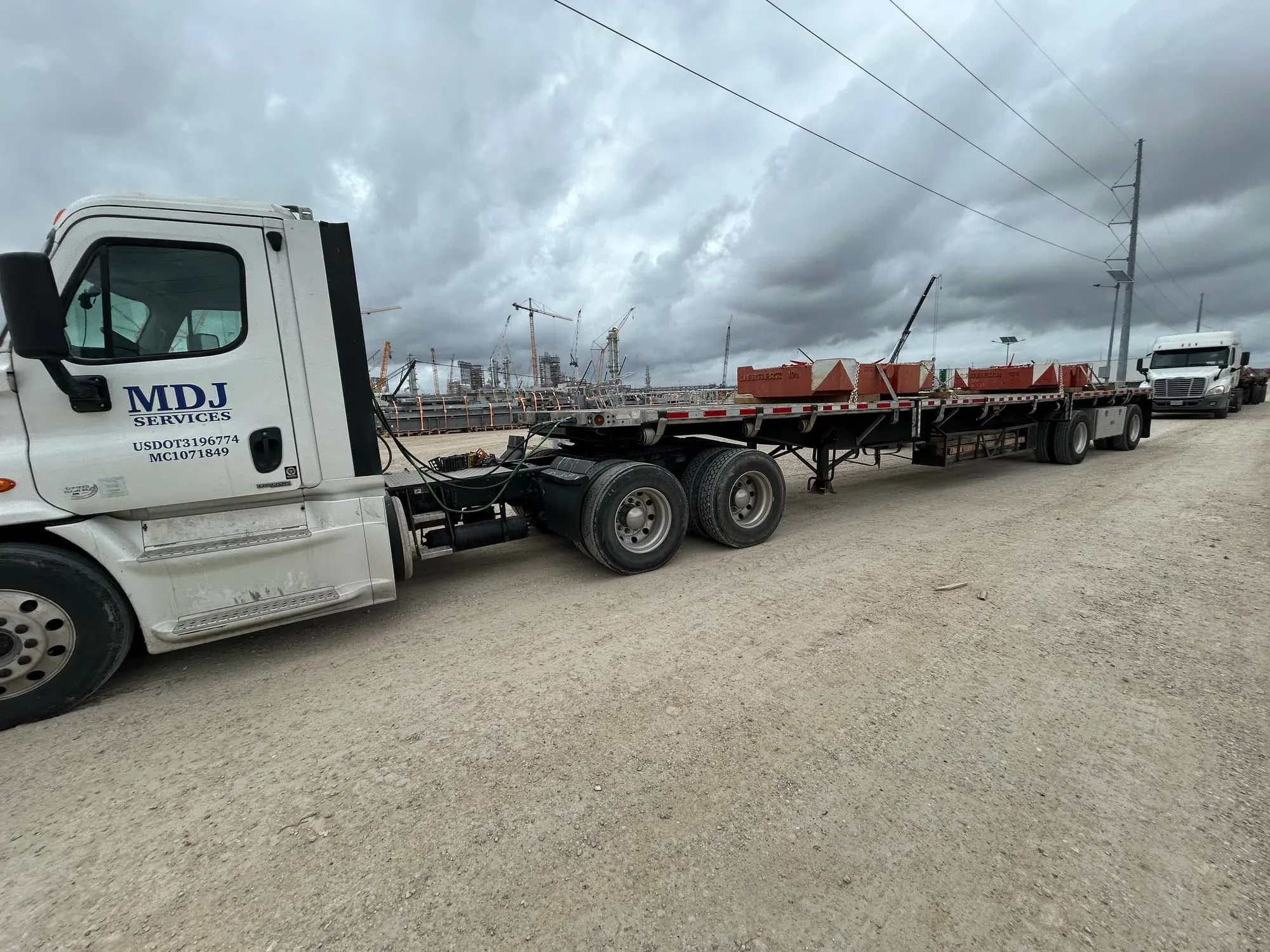 Crane counterweights chained to an MDJ Services flatbed at an industrial construction site in Southeast Texas